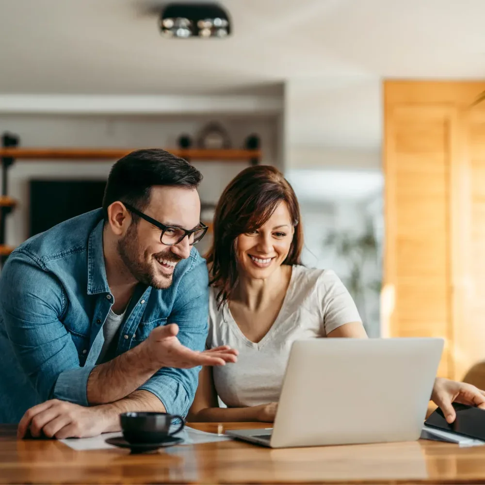 A couple smiling at a laptop at their kitchen table