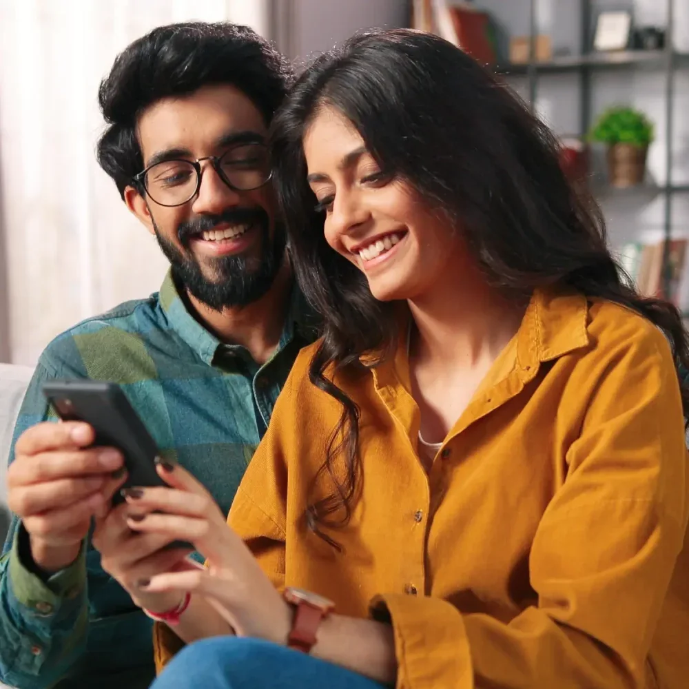 A couple smiling together at a phone on their couch